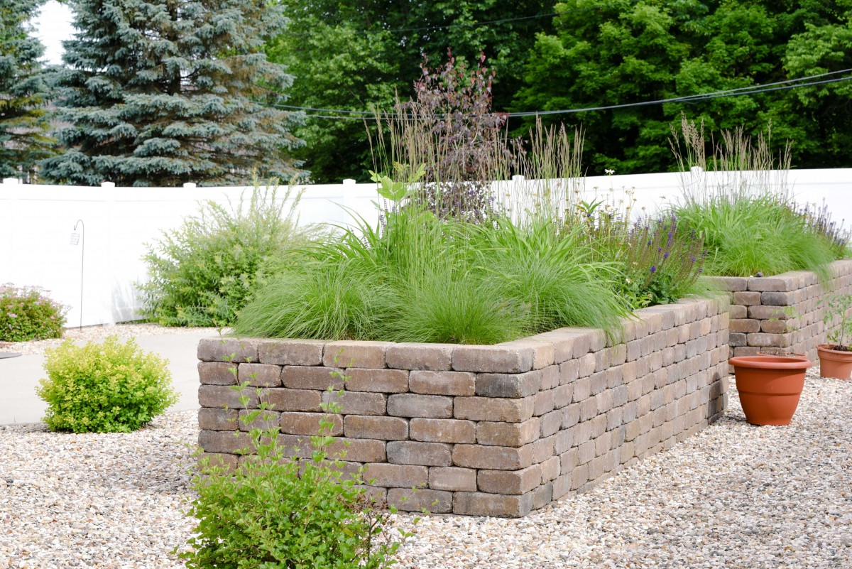 A landscaped garden featuring a brick retaining wall with various plants and greenery.