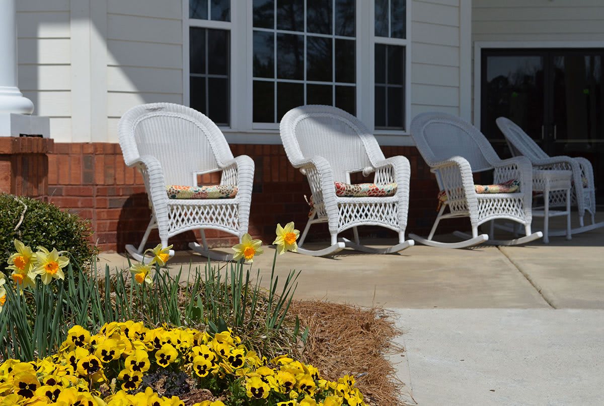 A cozy porch with white wicker rocking chairs and a vibrant bed of yellow flowers.