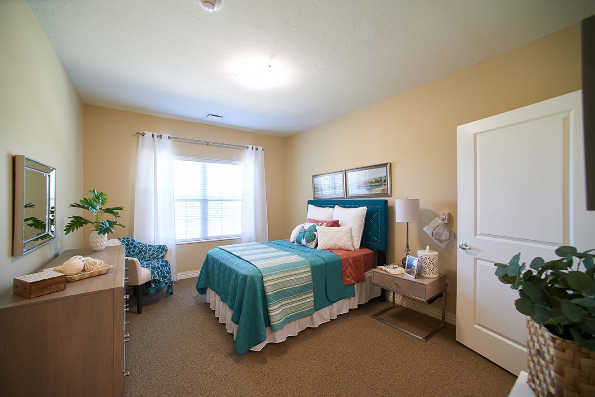 A cozy bedroom with teal and white bedding, complemented by neatly arranged furniture and decor.