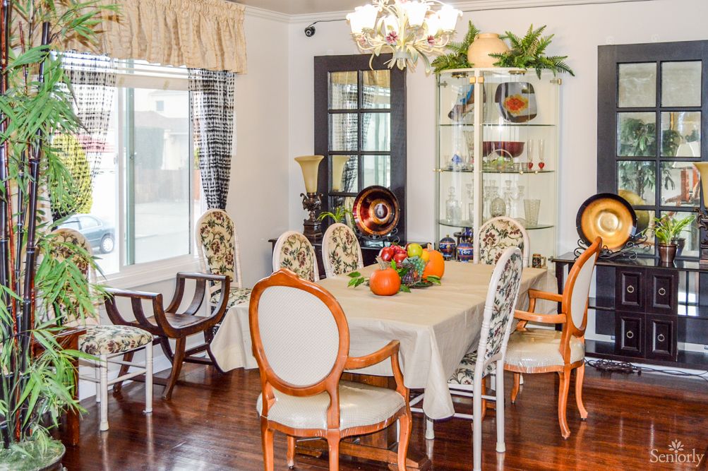 A well-decorated dining room featuring a table with a fruit bowl, surrounded by chairs and illuminated by a chandelier.