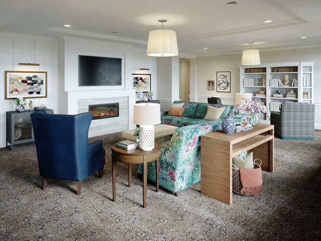 A cozy living room featuring a floral sofa, blue armchairs, and a fireplace with a mounted television.
