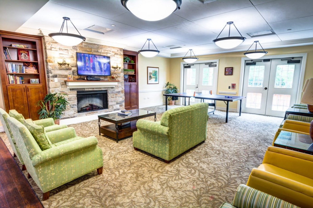 A cozy living room with green sofas, a television mounted above a fireplace, and elegant chandeliers.