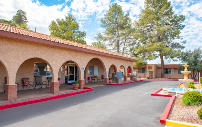 A sunny day at a motel featuring distinctive arches and a parking area surrounded by trees.