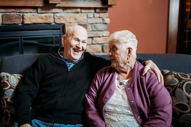 An elderly couple smiling warmly while sitting together in a cozy living room.