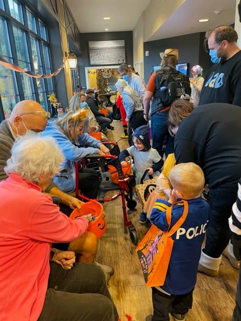 Children dressed in costumes participate in a Halloween trick-or-treat event indoors, engaging with adults handing out treats.