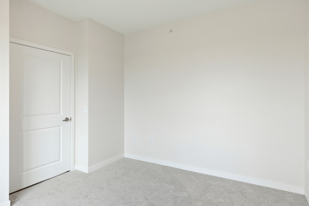 An empty room with white walls, a closed door, and carpeted floor.