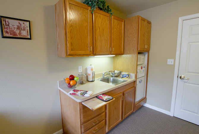 A compact kitchen setup featuring wooden cabinets, a sink, and a countertop with fruits and small appliances.