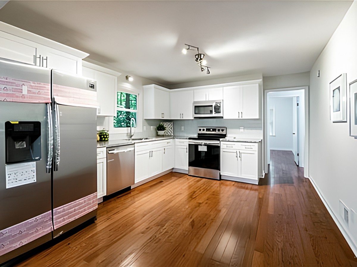 A modern kitchen with white cabinets and stainless steel appliances on a hardwood floor.
