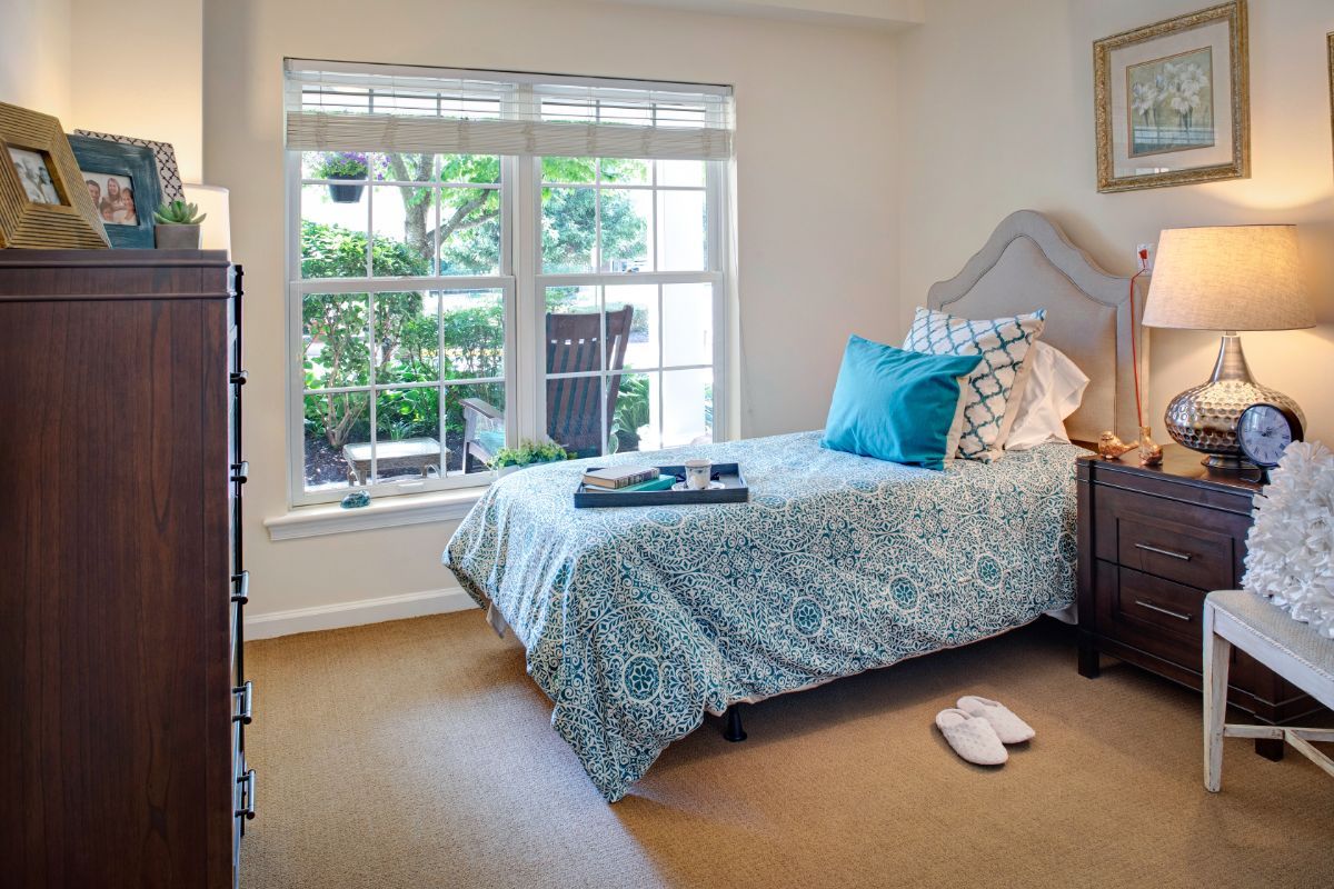 A cozy bedroom with a single bed, decorative pillows, and ample natural light from a large window providing a garden view.