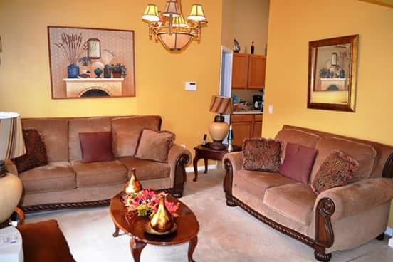 A cozy living room with brown sofas, a wooden coffee table, and yellow walls adorned with artwork.