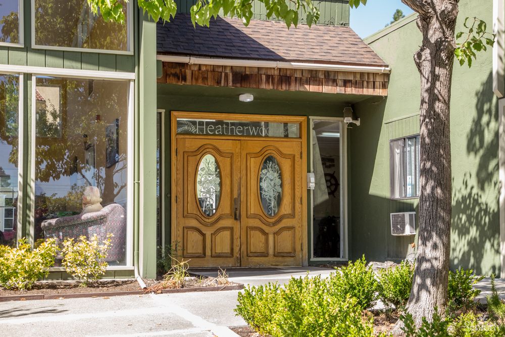 A wooden double door entrance to a building with plants in front.