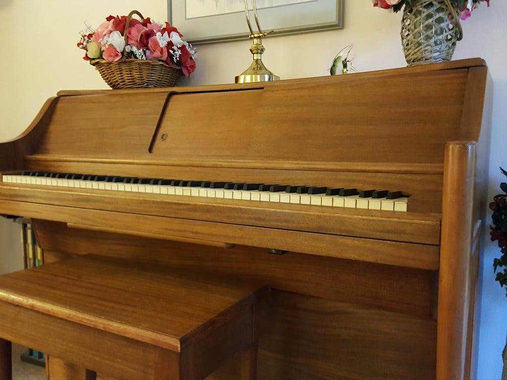 A wooden piano with a decorative floral arrangement on top, accompanied by a matching bench.