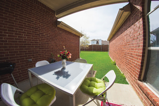 A cozy outdoor patio area featuring a modern table and stylish seating, surrounded by brick walls and a lush green lawn.
