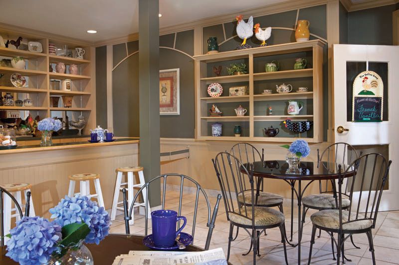 A cozy cafe with elegant interior design, featuring tables and chairs surrounded by decorative shelves and flowers.