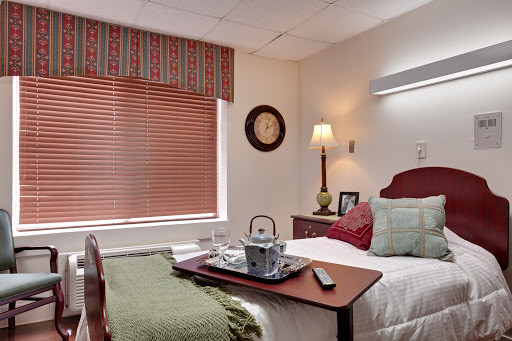A cozy hospital room featuring a neatly made bed, a bedside table with a tray, and warm lighting.