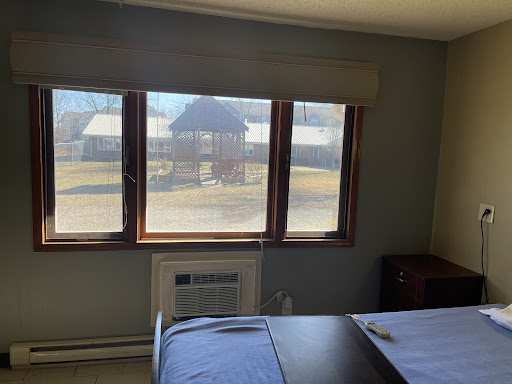 A cozy room featuring a large window with a view outside, an air conditioning unit, and simple furnishings.