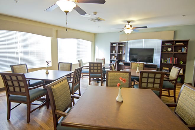 A well-lit dining area featuring tables and chairs, ceiling fans, and a vase with flowers on one of the tables.