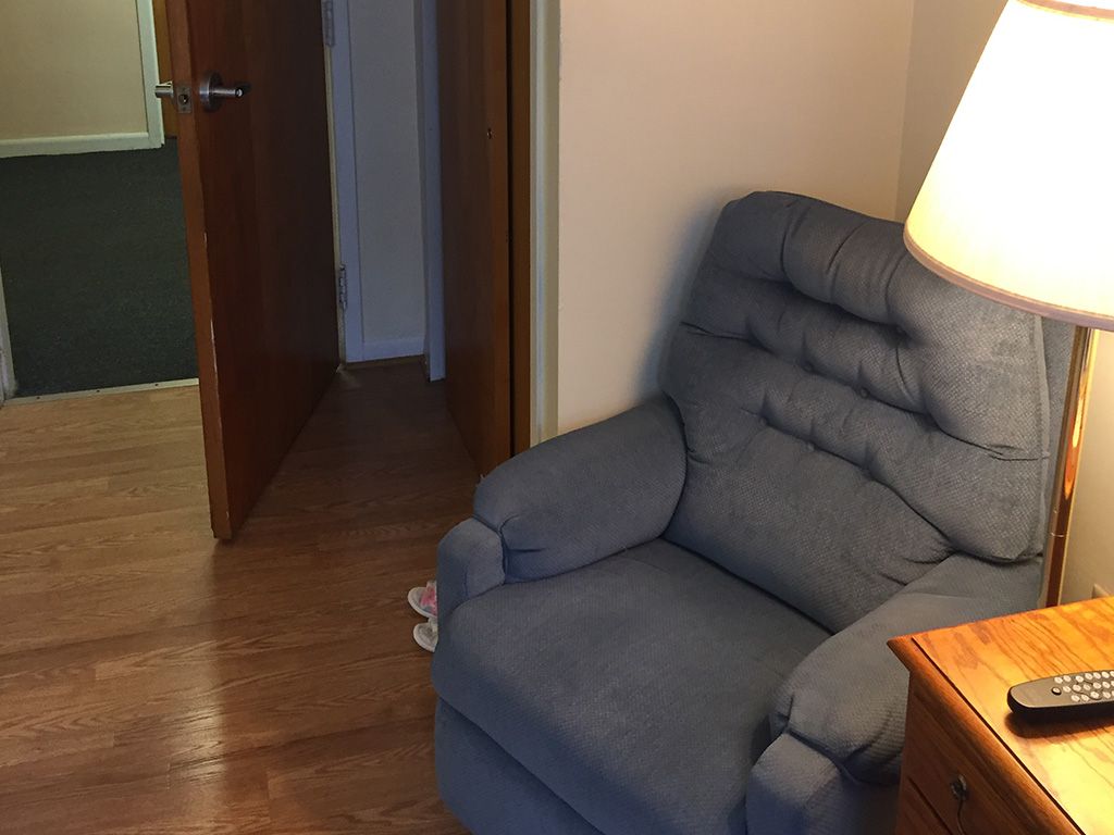 A cozy living room corner featuring a blue recliner next to a lamp and an open doorway.