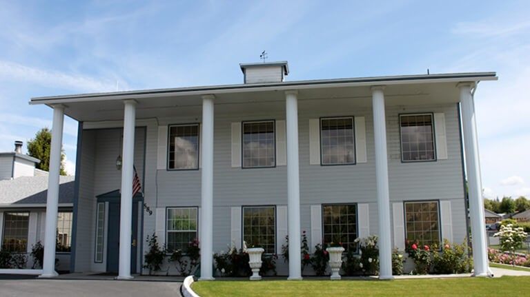 A two-story building with large columns and multiple windows against a blue sky.
