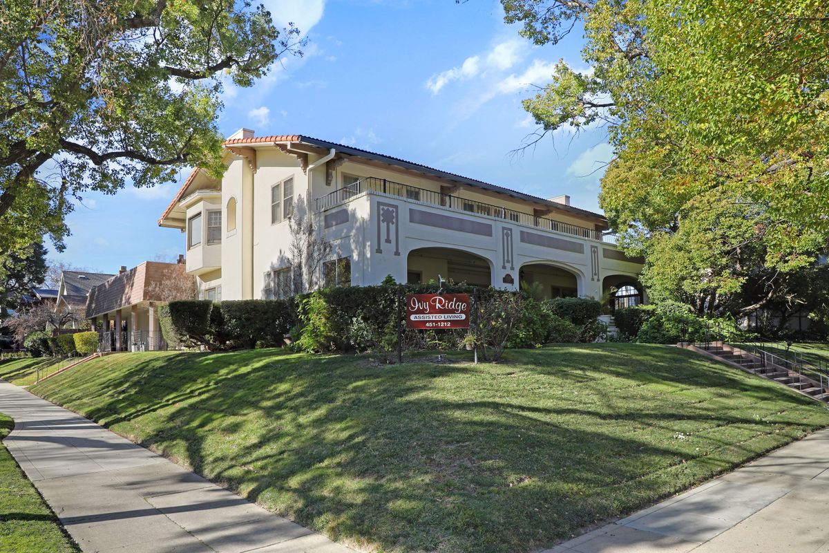A two-story residential building surrounded by lush greenery and a clear blue sky.