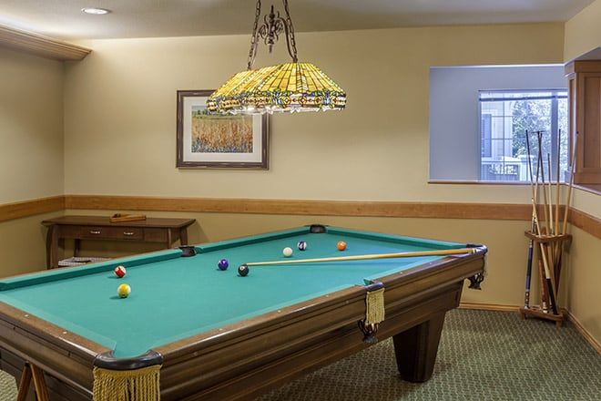 A cozy recreation room featuring a billiards table with cue sticks arranged on top, under a decorative hanging lamp.