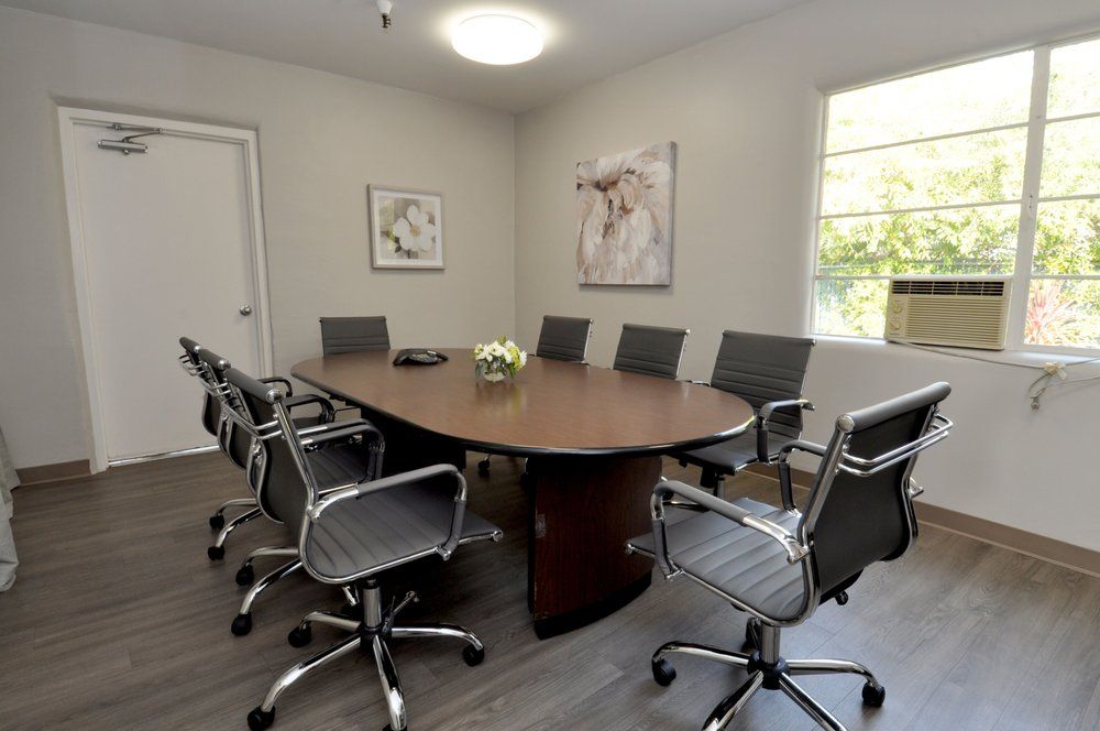 A modern conference room with a large wooden meeting table, surrounded by sleek office chairs and adorned with artwork on the walls.