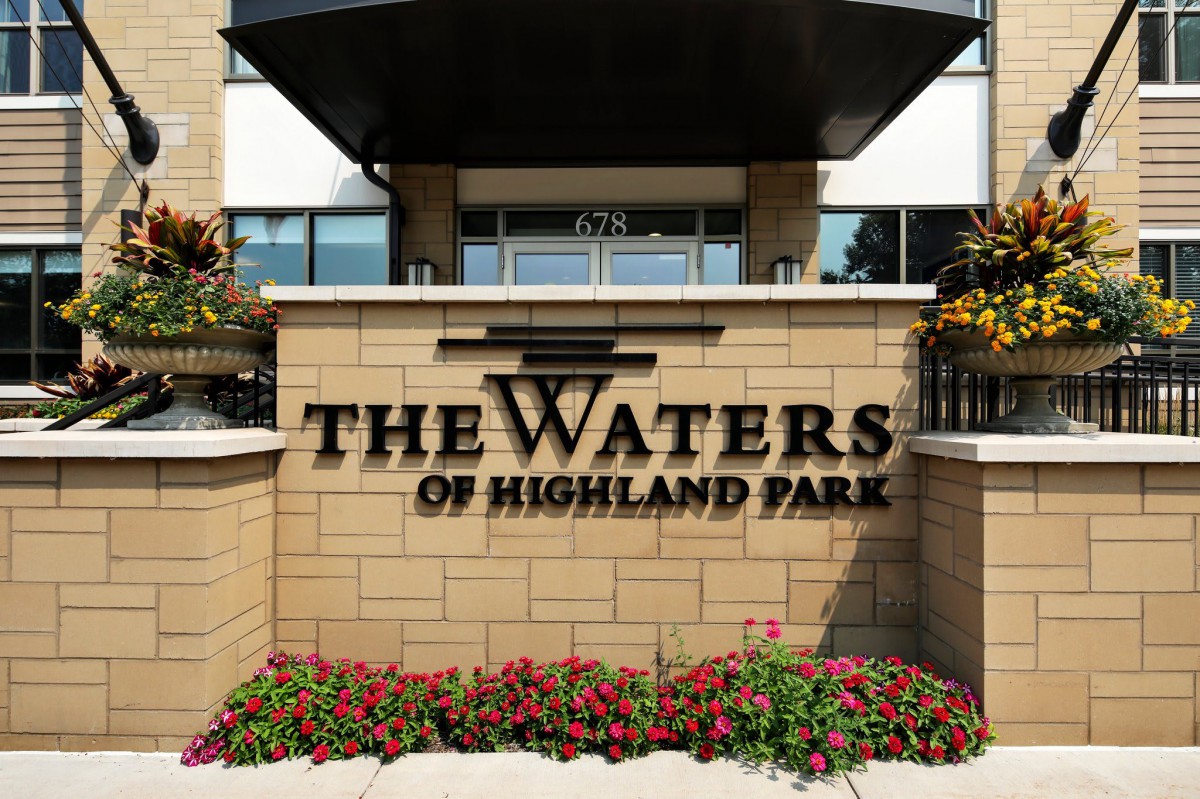 Entrance sign for The Waters of Highland Park, featuring landscaping with flowers.