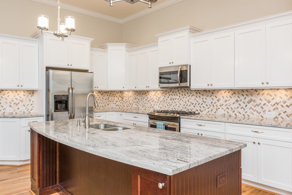 A modern kitchen featuring white cabinets, stainless steel appliances, and a large island with a marble countertop.