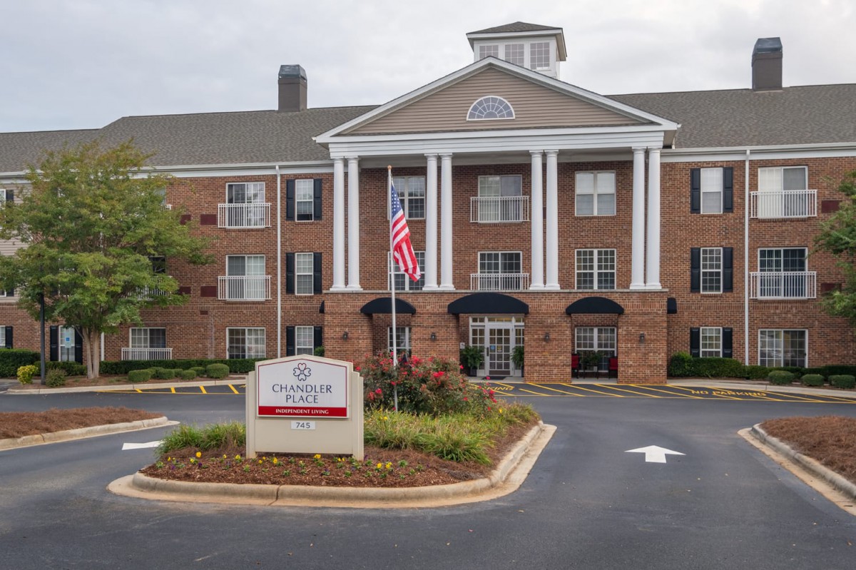 A brick retirement home with a classical design, featuring white columns and an American flag at the entrance.