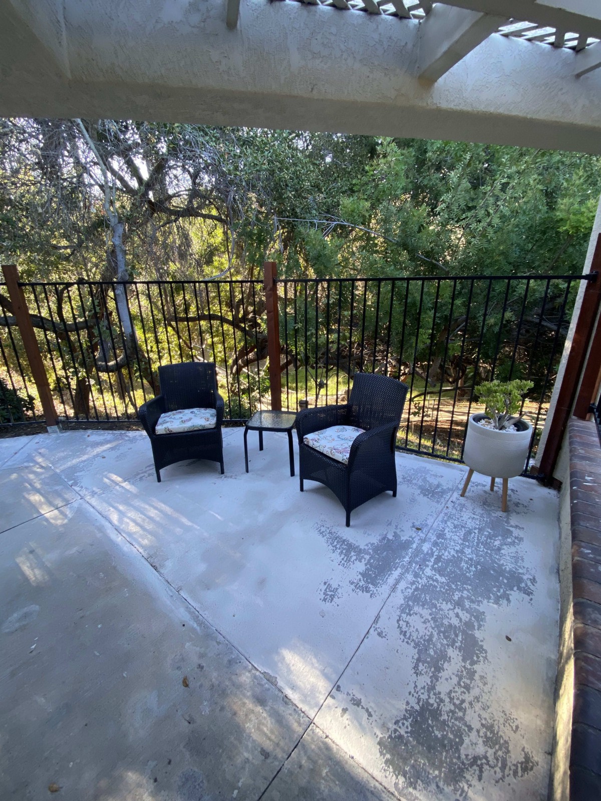 A cozy patio setup with two chairs, a table, and a plant, surrounded by trees and a fence.