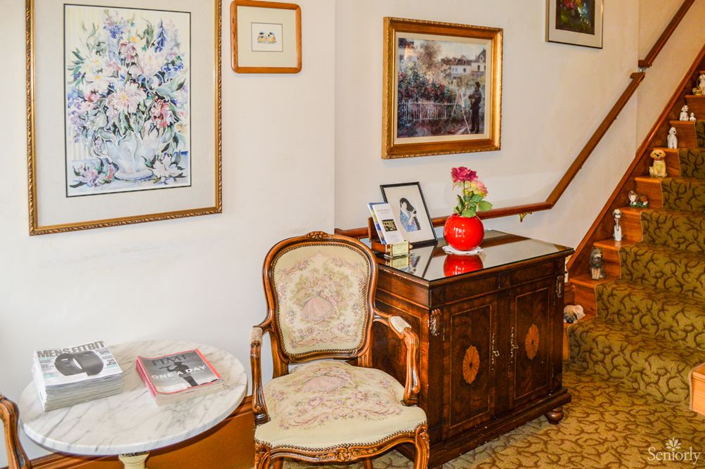 A cozy interior corner featuring framed artwork, an ornate chair, and a classic wooden table with decorative items.