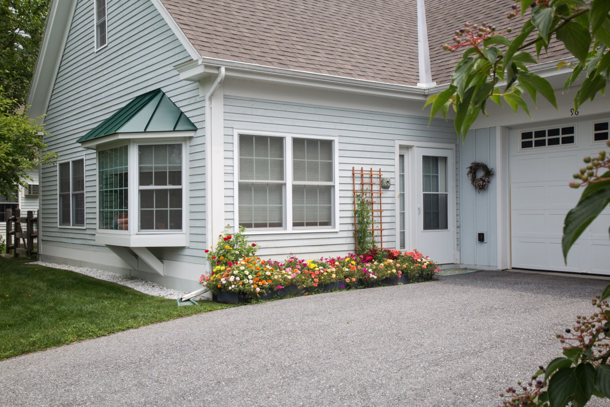 A charming house with a well-maintained flower garden and a driveway leading to the front door.
