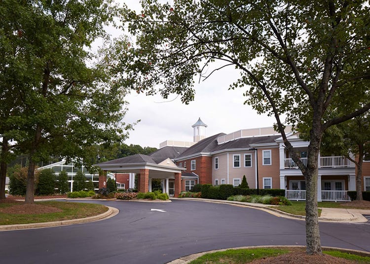 A view of a well-maintained building with a driveway and surrounding trees.