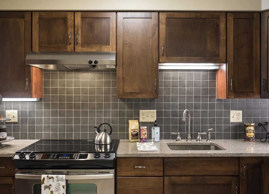 A cozy kitchen with wooden cabinets, a stainless steel stove and kettle, and a tiled backsplash.
