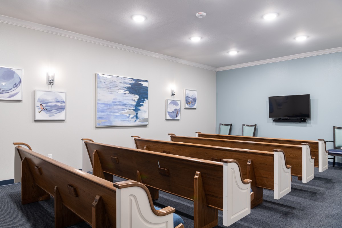 An interior view of a small room with wooden church pews, artwork on the walls, and ceiling lights.