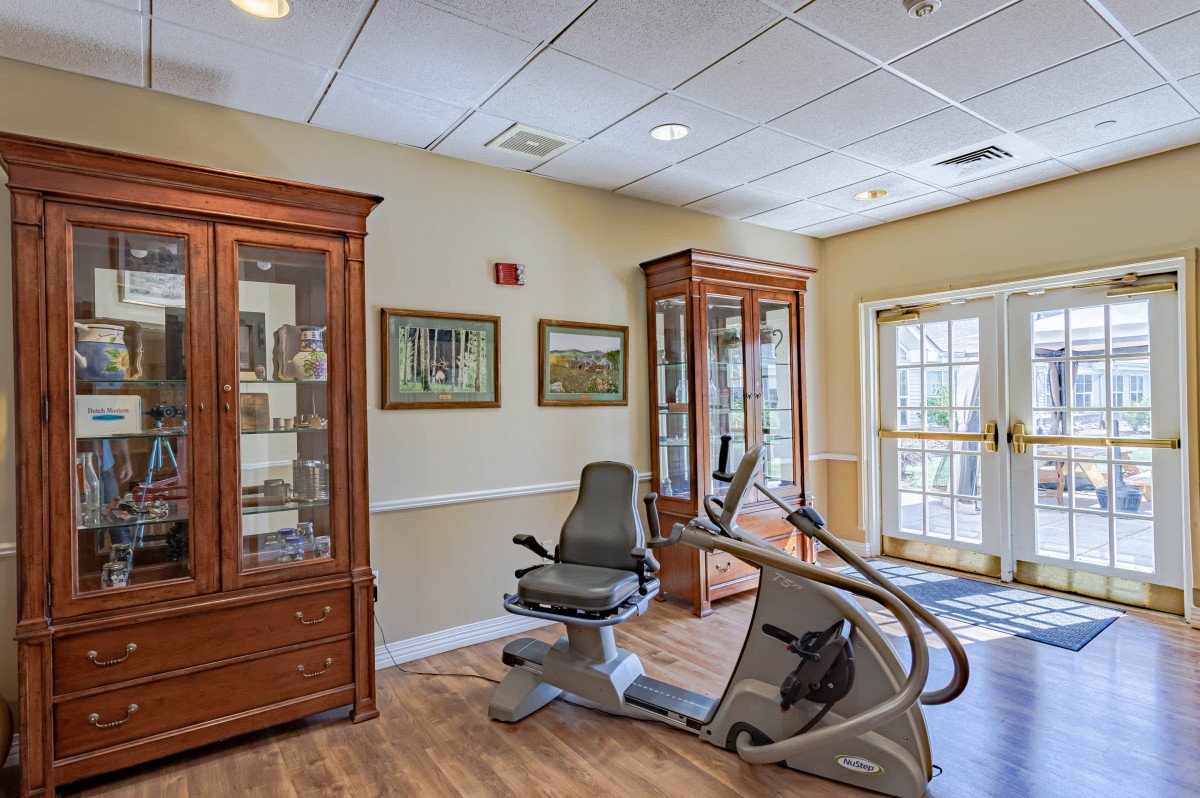 A well-decorated room featuring an exercise bike, framed artwork, and wooden display cabinets.