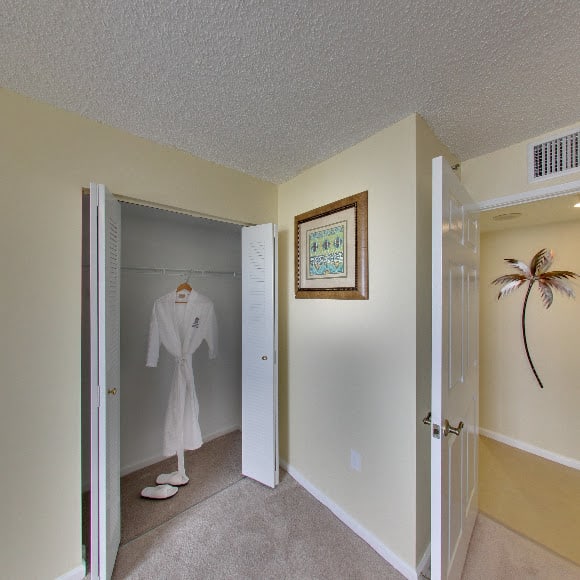 A view of a small hallway with an open closet containing a white robe and framed artwork on the walls.