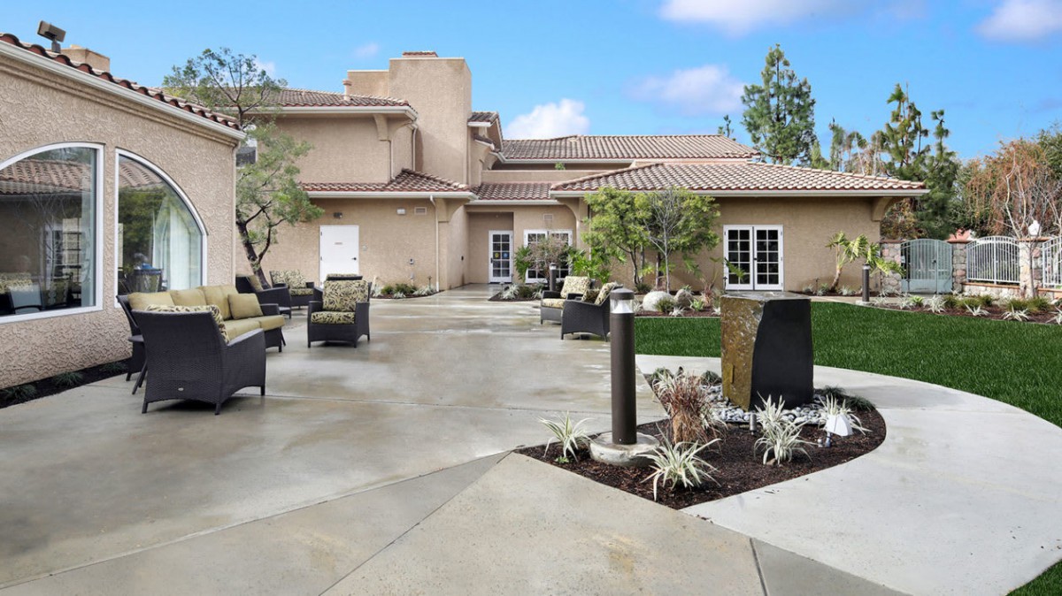 A well-designed outdoor patio area with modern furniture and landscaping, set against a building and a clear sky.