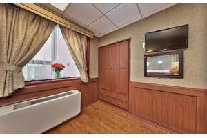 A cozy room featuring wooden paneling, a window with curtains, and a wall-mounted television.