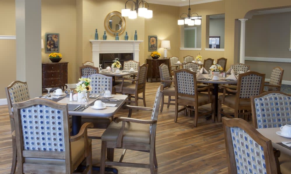 A cozy dining room with neatly arranged tables and chairs, featuring a warm fireplace and elegant chandeliers.