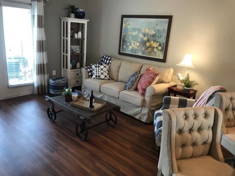 A cozy living room with a beige sofa, patterned cushions, a rustic coffee table, and decorative elements including a painting and lamp.