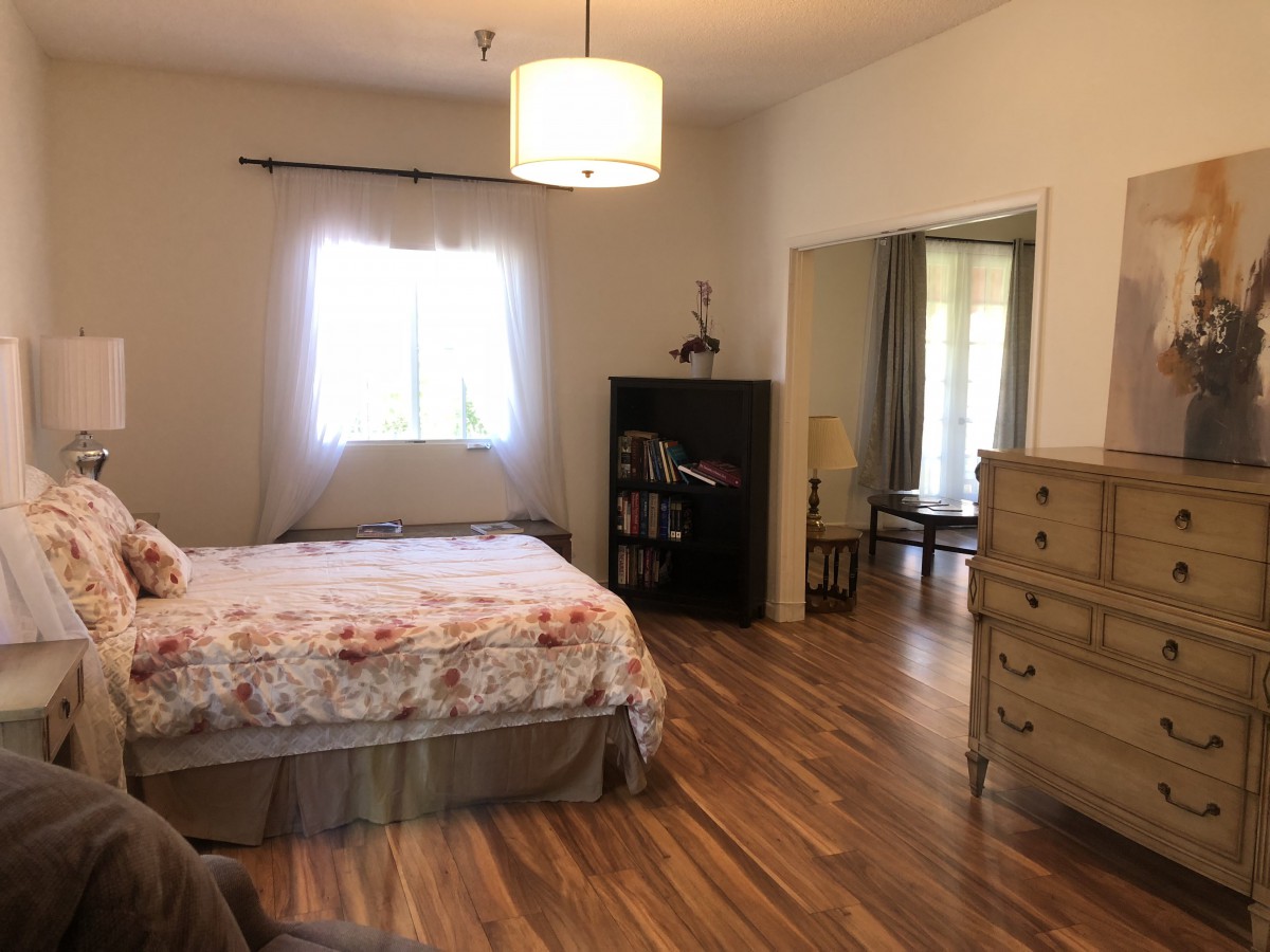 A cozy bedroom with wooden flooring, featuring a bed, dresser, and bookshelf.
