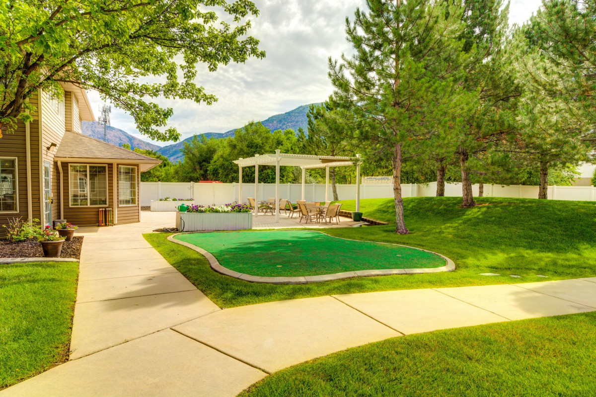 A serene backyard with a green lawn, trees, and a pavilion set against a mountain backdrop.