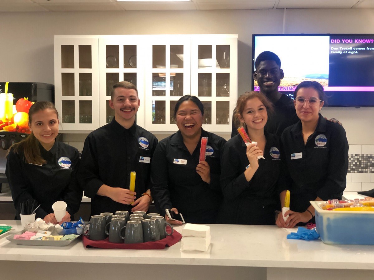 A team of smiling people in uniforms preparing food in a kitchen.