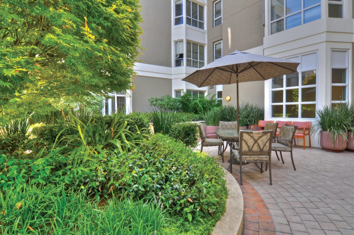A serene outdoor patio area with garden greenery and seating under an umbrella.