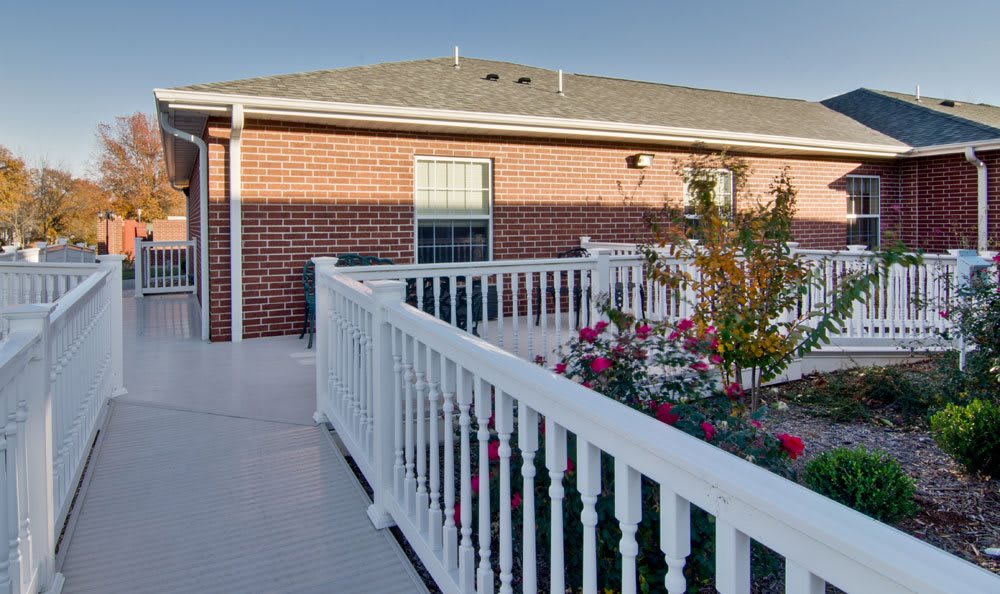 A sunny outdoor view of a building with brick walls, surrounded by a white fence and colorful flowers.
