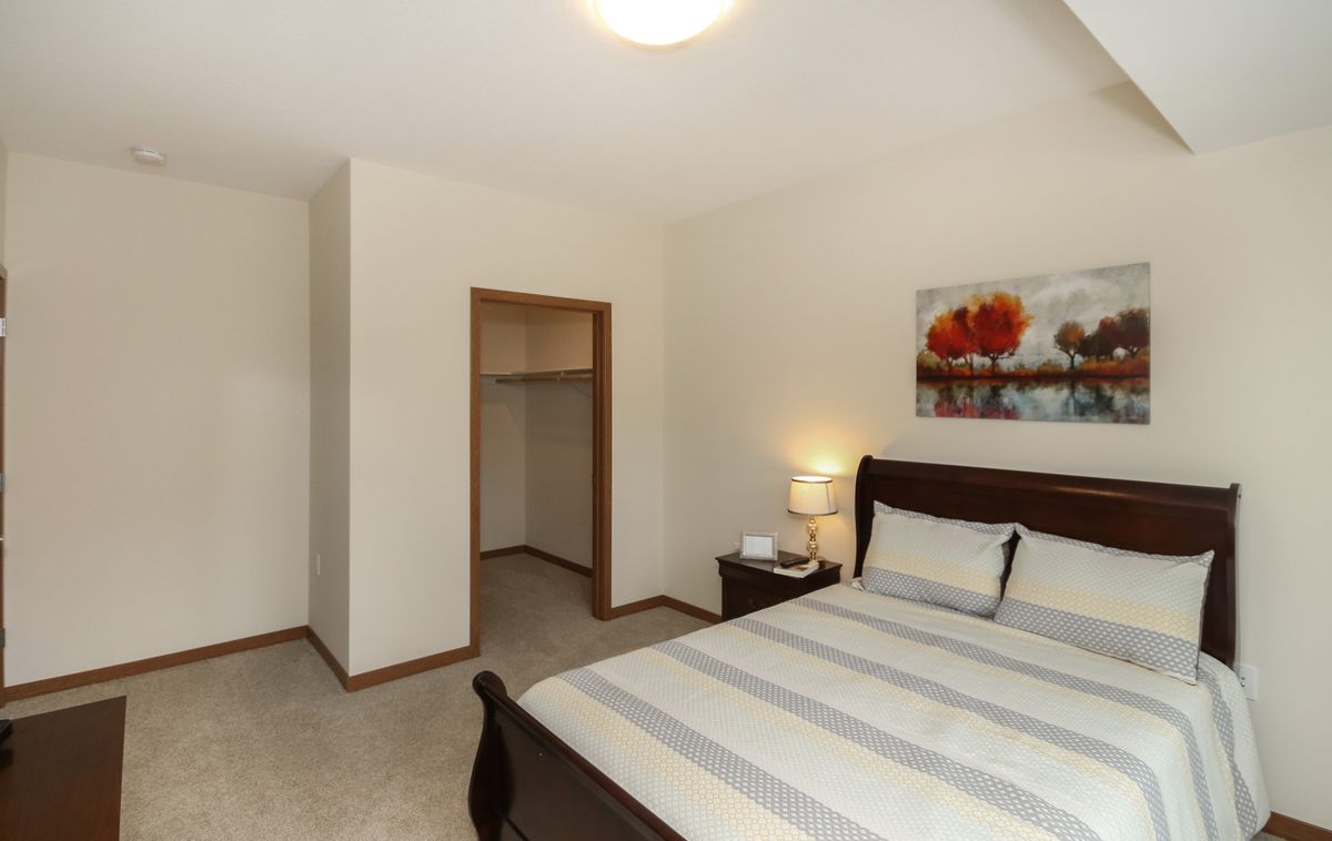 A cozy bedroom with a neatly made bed, a bedside lamp, and an open closet.