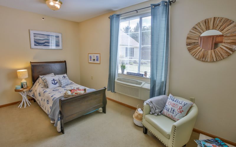 A bright and cozy child's bedroom with a bed, chair, and large window.