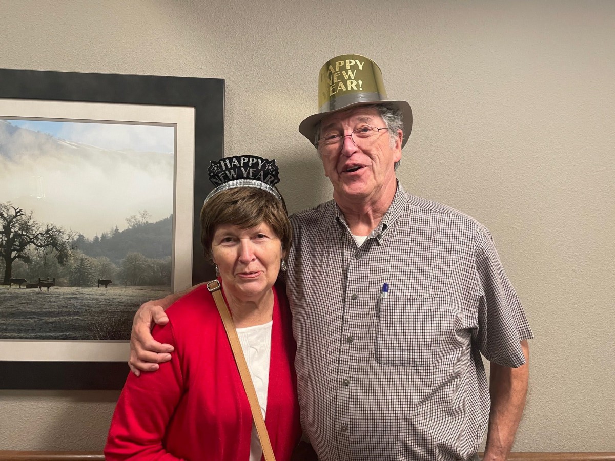 An elderly couple wearing New Year party hats indoors, celebrating together.
