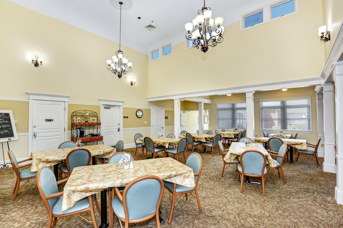 A spacious dining area with multiple tables and chairs, illuminated by elegant chandeliers.